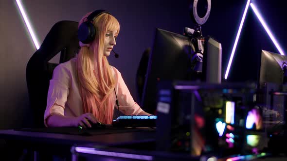 Indoor Shot in a Dark Gaming Room with Neons of a Longhaired Blonde Focused Caucasian Woman Playing