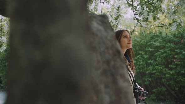 Young woman walking under blossoming tree while touching the branches