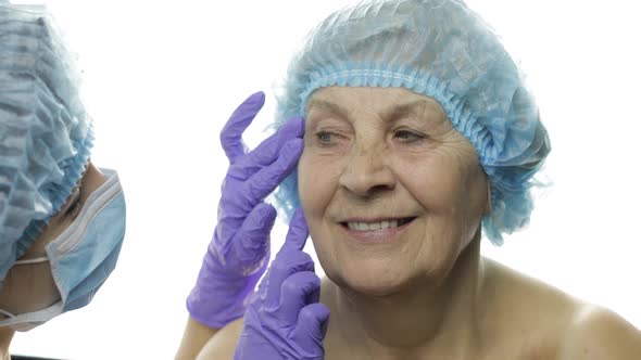 Smiling Elderly Female in Protective Hat. Plastic Surgeon Checking Woman Face