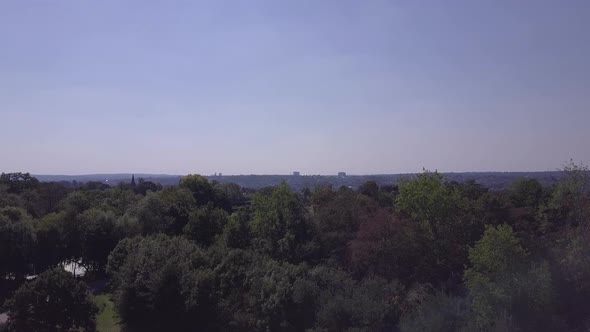 Drone aerial view flying up with row of trees in foreground revealing North London skyline. Filmed i