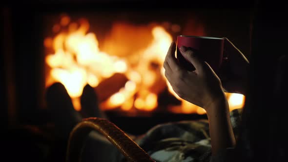 Tea By the Fireplace Female Hands with a Red Cup on the Background of the Fireplace Where the Fire