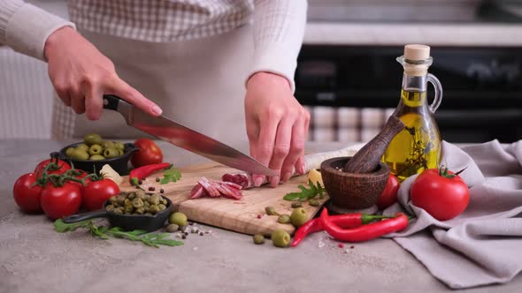 Woman Slicing Fuet Sausage with Knife at Domestic Kitchen