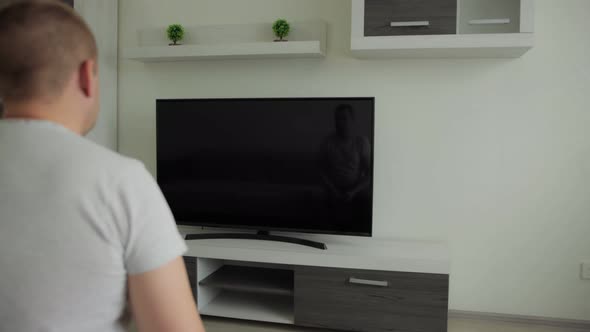 Man Sits at Home in Hall Room and Watches Movie on Lcd TV