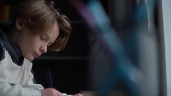 Closeup Face of Serious Focused Smart Child Schoolboy Doing Homework Writing to Notebook with Pen