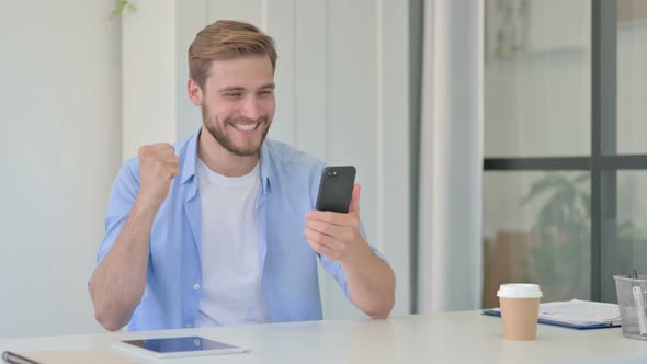 Young Creative Man Celebrating Success on Smartphone in Office