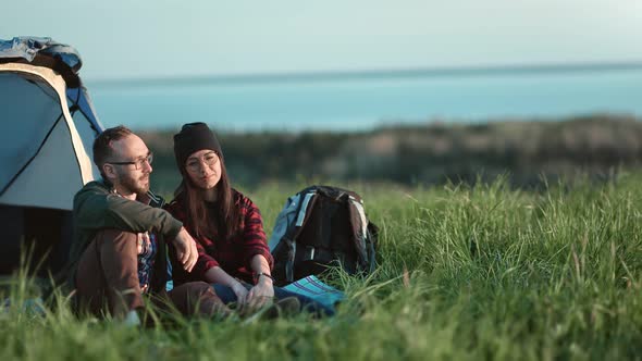 Relaxed Couple Sitting on Grass at Camping Tent Admiring Landscape