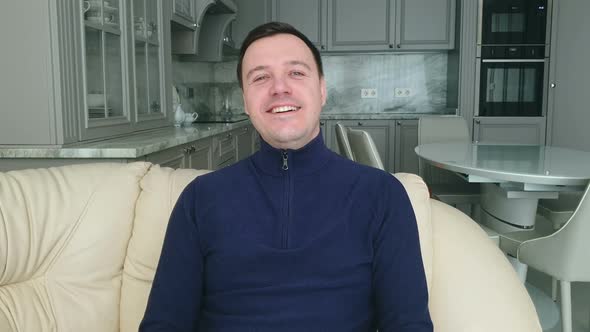 Young adult man sitting on sofa at home and looking at camera and Smiling