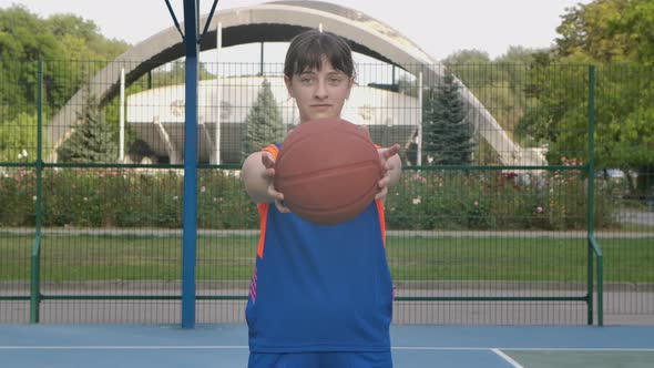 Portrait of a Young Girl Who Looks at the Camera and Stretches Forward a Basketball. A Teenager in