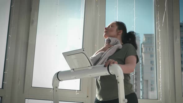 Portrait of chubby woman is wiping sweat with towel while walking on treadmill