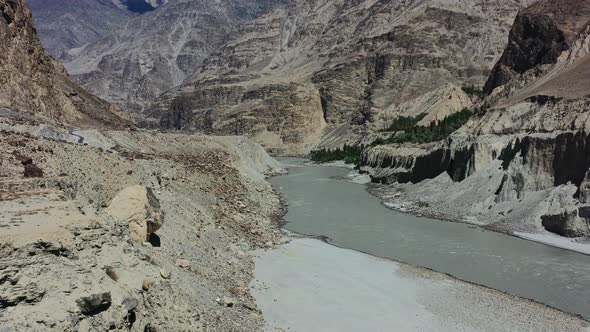 aerial drone flying over a mountain cliff towards the fast flowing gray Indus River in Skardu Pakist
