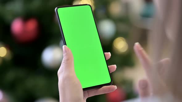 Female Hand Holding Chroma Key Screen Smartphone Near Christmas Tree