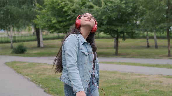 Beautiful Cheerful Girl Dancing in the Park Listening To Music on Headphones