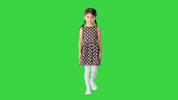 Little Girl in Polka Dot Dress with Pig Tails Walking and Smiling Shyly To the Camera on a Green