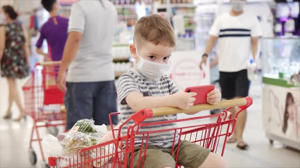 Family Makes Purchases in the Hypermarket, the Child Sits in a Protective Mask From Viruses, Watches