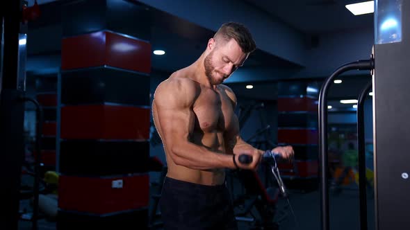 Handsome strong young bodybuilder works out on sport equipment. Strong abs. Modern gym background.