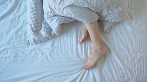 Female Legs in the Bed Under Blanket