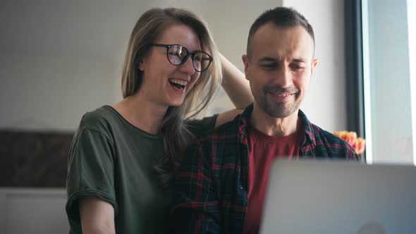 Happy Young Adult Couple Using a Laptop Doing Online Shopping Together