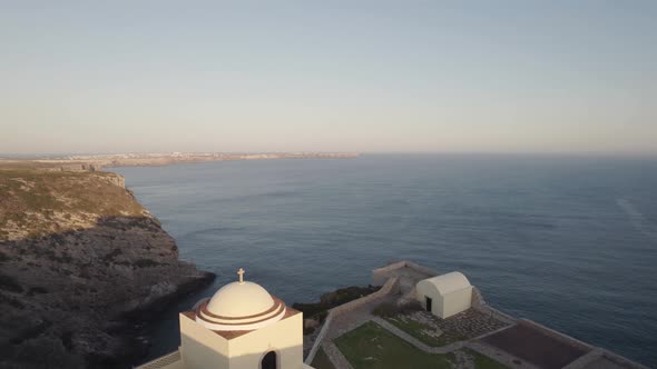 Drone flying out from cliffside chapel from fort of Santo António de Belixe