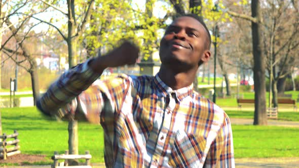 A Young Black Man Celebrates in a Park on a Sunny Day
