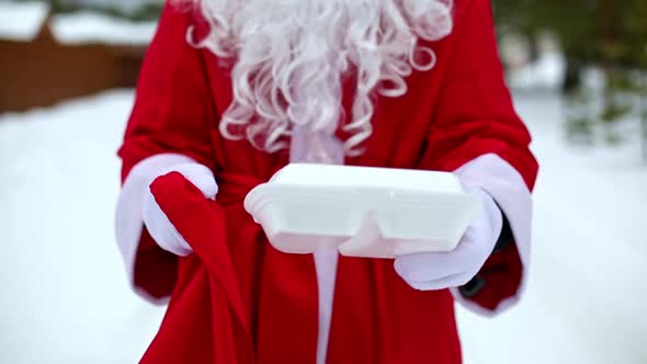 Food delivery service containers in hands of Santa Claus outdoor in snow. Christmas eve promotion. R