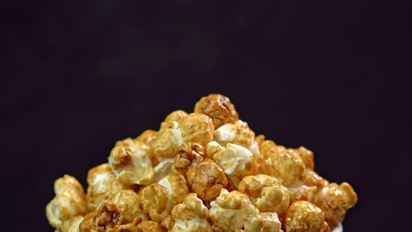 Coffee taste popcorns rotating into the bowl on black background close up. Caramel popcorn. Health