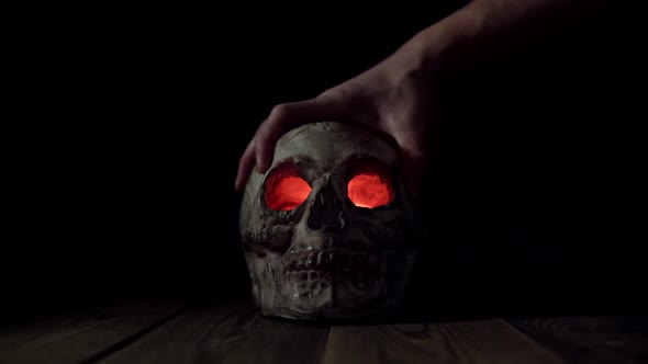 Man Puts His Hand on a Human Skull with Glowing Eyes and Smoke Coming Out of Them