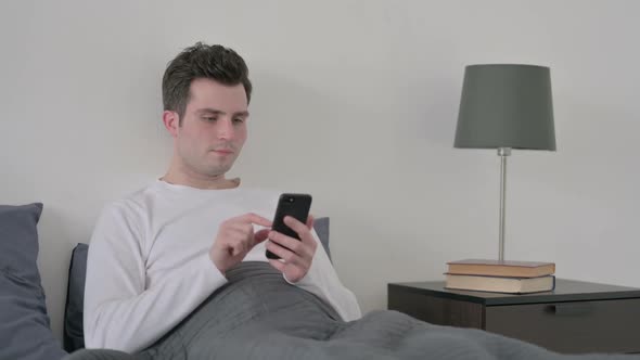 Man Celebrating Success on Smartphone in Bed