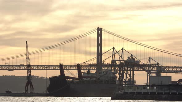 25Th April Bridge Tejo's River with construction cranes and road traffic in the sunset with an aband