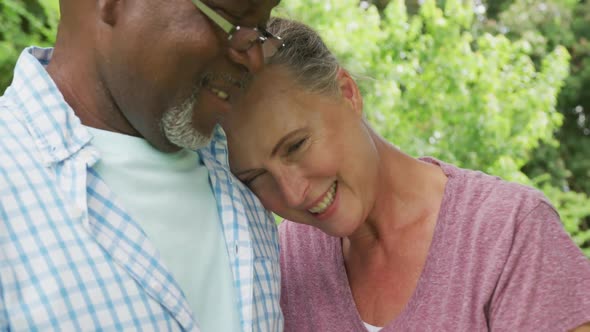 Happy senior diverse couple wearing shirts and embracing in garden