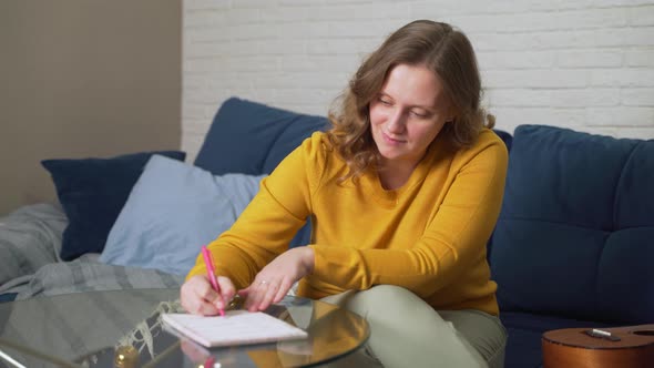 Woman is Writing Something on Sheets of Paper at Glass Table with Pen