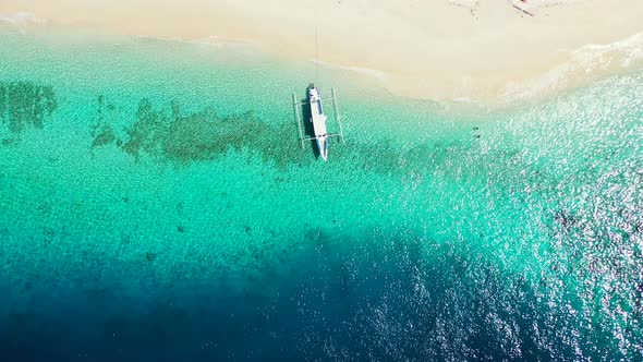 Anchored boat floating on clear water of turquoise lagoon which flows on white sand of exotic beach,