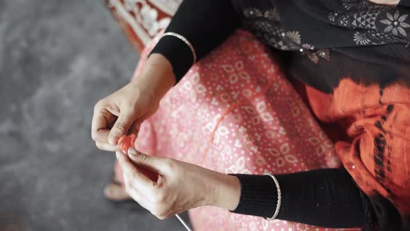 Directly above footage of Indian woman's hands knitting with red wool and needle crafts.