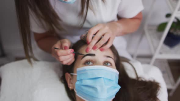 Caucasian woman wearing face mask lying down having eyebrows dyed