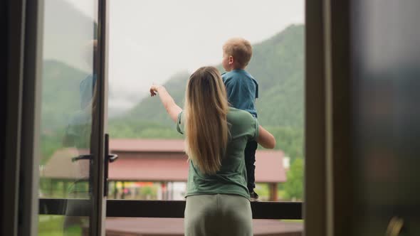 Careful Mother Shows Green Hills Holding Son on Balcony