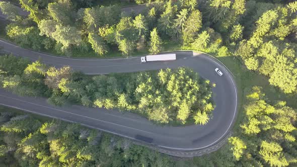 Aerial view of winding road with mowing cars and trucks in high mountain pass trough dense woods.