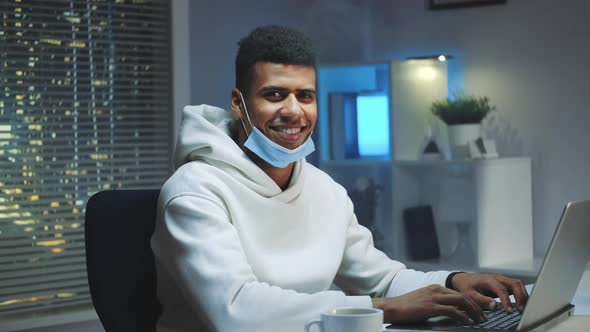 Handsome Black Man with Medical Mask Smiling to the Camera While Working Home