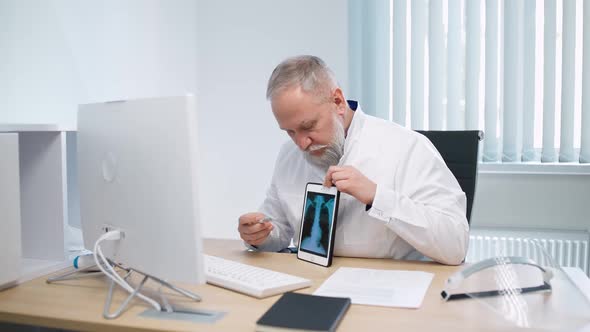 Grayhaired Male Doctor Sits at Workplace and Communicates with Patient Via Video Call the Doctor