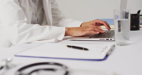 Video of biracial female doctor using laptop on blue background