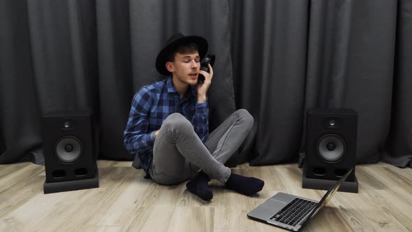 Man listening to music in headphones wearing black hat looking at laptop in home music studio