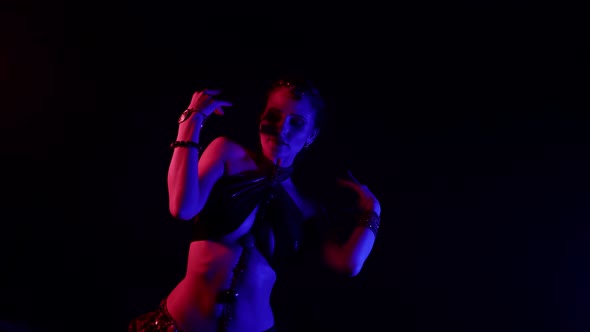 Alluring Woman is Performing Exotic Oriental Dance in Dark Studio with Red Blue Lights