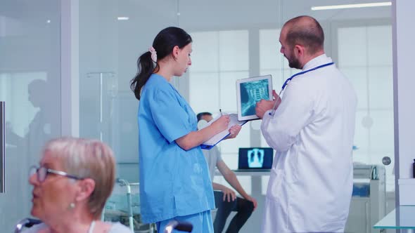 Medical Staff Holding Tablet Pc with Patient Radiography in Hospital Hallway