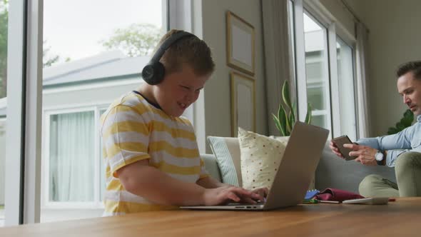 Caucasian father with son sitting in living room, using laptop and smartphone