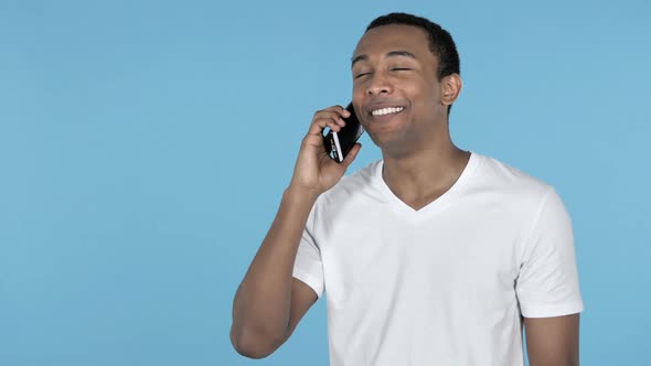 Young African Man Talking on Smartphone Blue Background