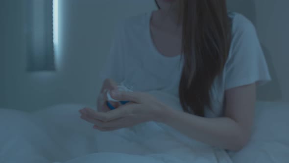 Asian unhappy sick girl in pajamas take medicine before sleep on bed.