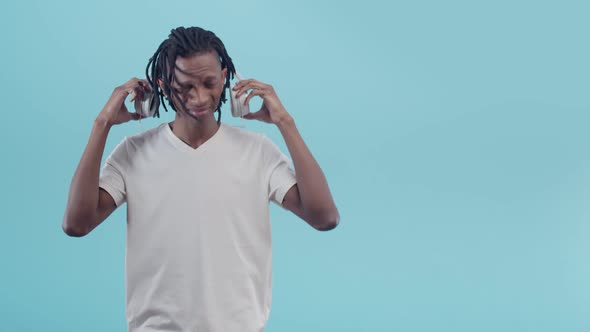 Black Unhappy Man with Dreadlocks Takes Off Headphones and Spreads Hands to the Sides Standing on a
