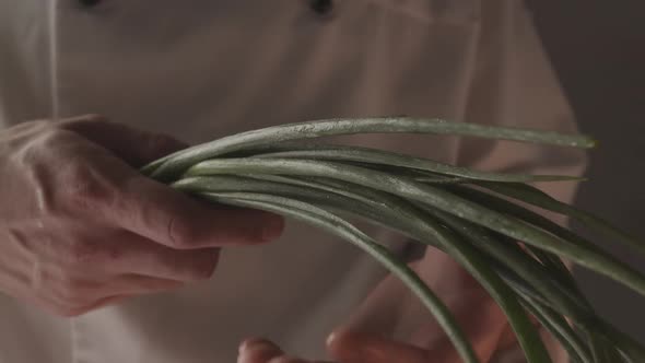 Chef in Uniform Works in the Kitchen and Holds Green Onions in His Hand