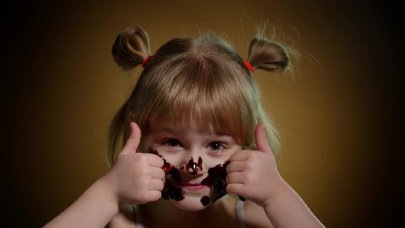 Portrait of Teen Smiling Child Kid Girl Smears Face with Melted Chocolate and Showing Thumbs Up Sign