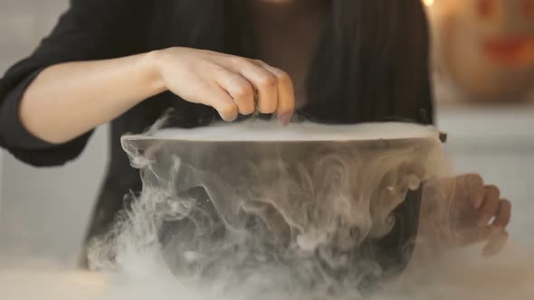 Witch Conjuring, Putting Magic Spell and Cooking Potion in Pot With White Smoke