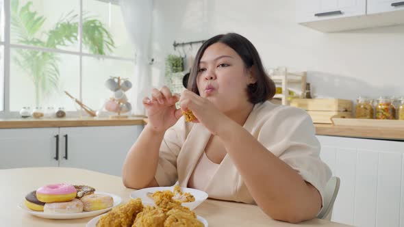 Asian plus size fat girl feeling hungry and happy to bite fried chicken and sweet donut on table.