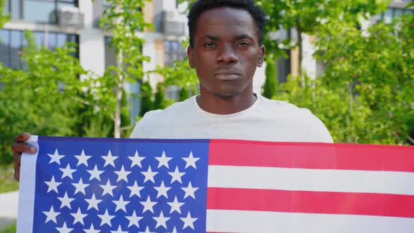 Camera Zoom in Afroamerican Man Holding an American Flag and Looks Camera